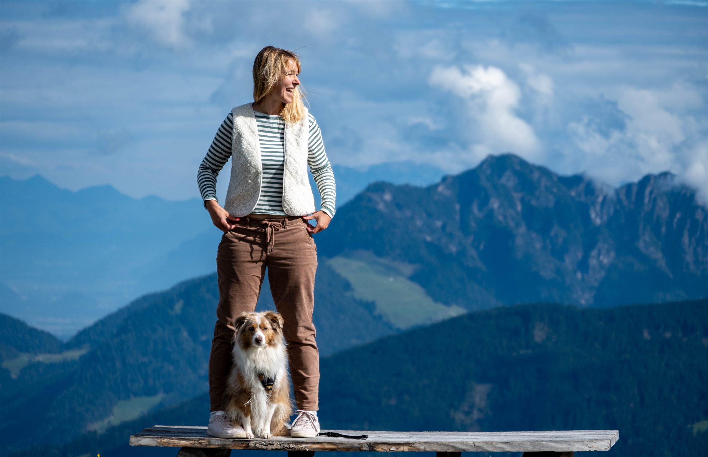 Julia Doubrawa mit ihrem Australian Shepherd Einstein auf einer Holzbank vor Bergpanorama