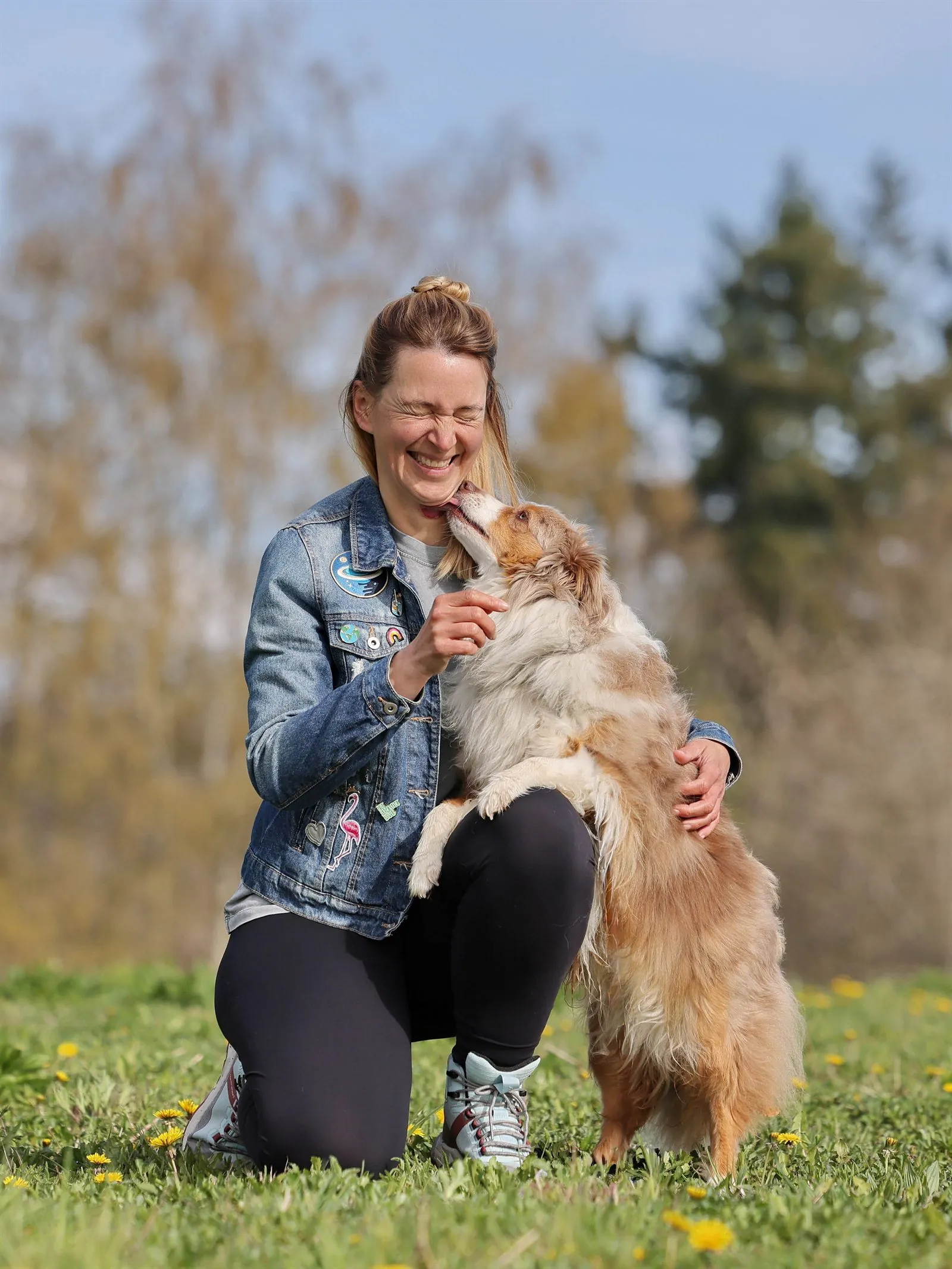 Julia Doubrawa kniet auf einer Wiese, ihr Australian Shepherd Einstein schmiegt sich an sie