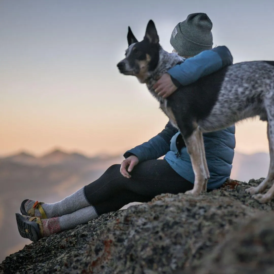Frau sitzt mit ihrem Hund auf einem Felsen vor Bergpanorama im Abendlicht