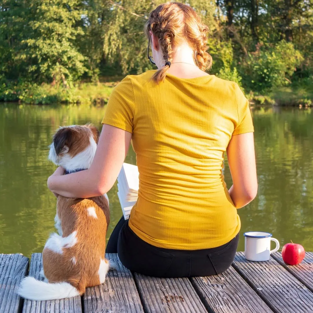 Frau sitzt mit ihrem Hund auf einem Steg am See